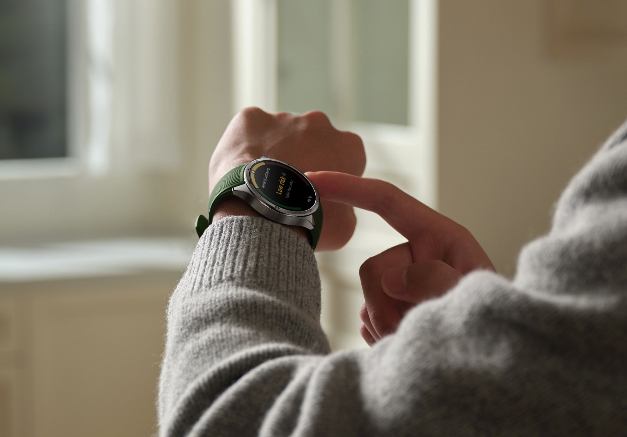 A person wearing a gray sweater and using a green smartwatch with a screen displaying information.
